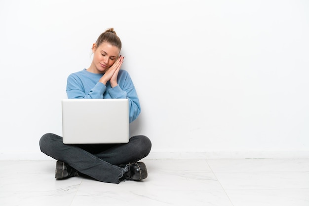 Junge Frau mit einem Laptop, der auf dem Boden sitzt und Schlafgeste in entzückender Ausdrucksweise macht