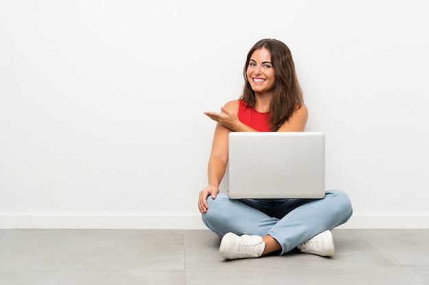 Junge Frau mit einem Laptop, der auf den ausdehnenden Händen des Bodens zur Seite sitzt