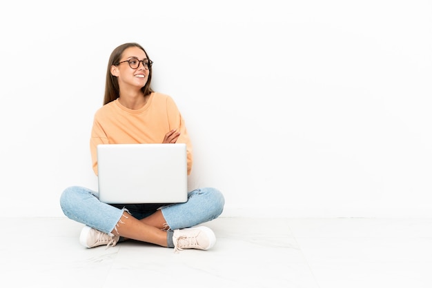 Junge Frau mit einem Laptop, der glücklich und lächelnd auf dem Boden sitzt