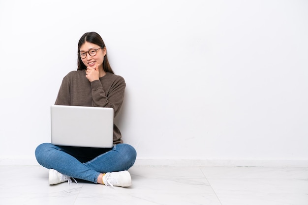 Junge Frau mit einem Laptop, der mit Brille auf dem Boden sitzt und lächelt