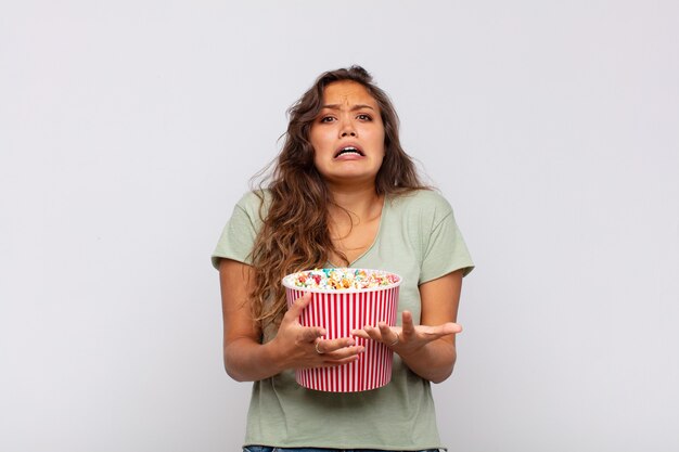 Junge Frau mit einem Pop conrs Eimer, der verzweifelt und frustriert, gestresst, unglücklich und genervt aussieht, schreit und schreit