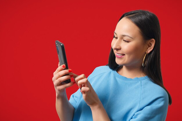 Junge Frau mit einem Smartphone auf rotem Grund.