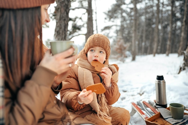 Junge Frau mit einem Sohn im Winterwald auf einem Picknick trinken heißen Tee