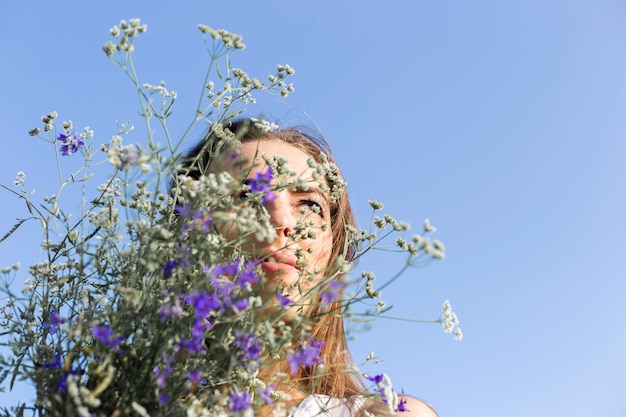 Junge Frau mit einem Strauß Wildblumen auf blauem Himmelshintergrund.