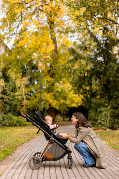 Junge Frau mit einem süßen Baby im Kinderwagen im Herbstpark