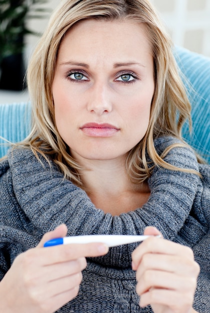 Junge Frau mit einem Thermometer, der die Kamera liegt auf einem Sofa betrachtet