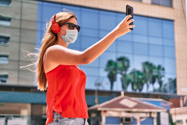 Junge Frau mit einer Maske, die ihr Handy in der Stadt benutzt Konzept der neuen Normalität und des Kampfes gegen das Virus.