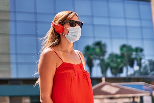 Junge Frau mit einer Maske, die Musik in der Stadt hört