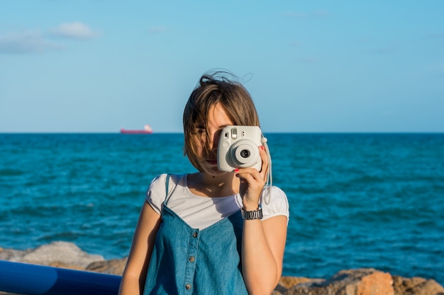 Junge Frau mit einer Sofortbildkamera in der Küste