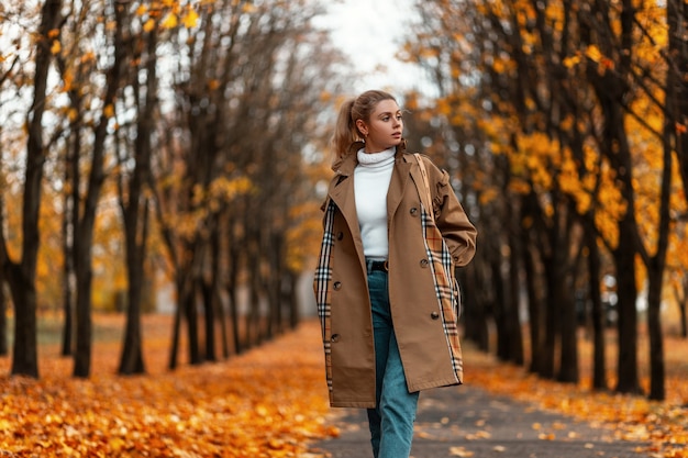 junge Frau mit einer trendigen Frisur in einem eleganten Mantel posiert im Freien in einem Park