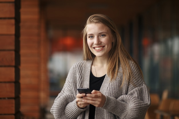 Junge Frau mit Einkaufstasche, die Telefon am sonnigen Herbsttag betrachtet.