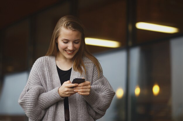 Junge Frau mit Einkaufstasche, die Telefon am sonnigen Herbsttag betrachtet.