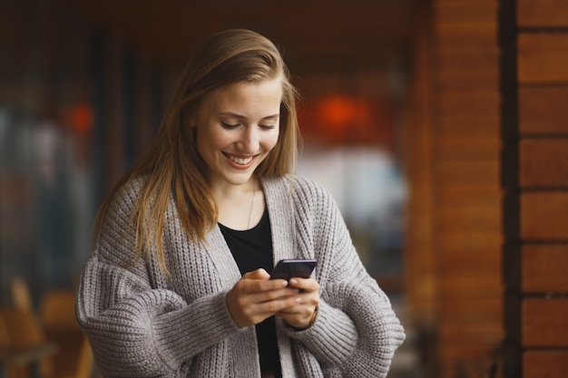 Junge Frau mit Einkaufstasche, die Telefon am sonnigen Herbsttag betrachtet.