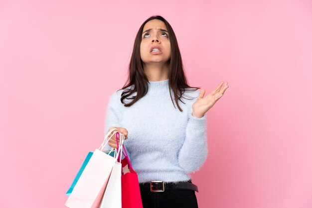Junge Frau mit Einkaufstasche über der lokalisierten rosa Wand frustriert durch eine schlechte Situation