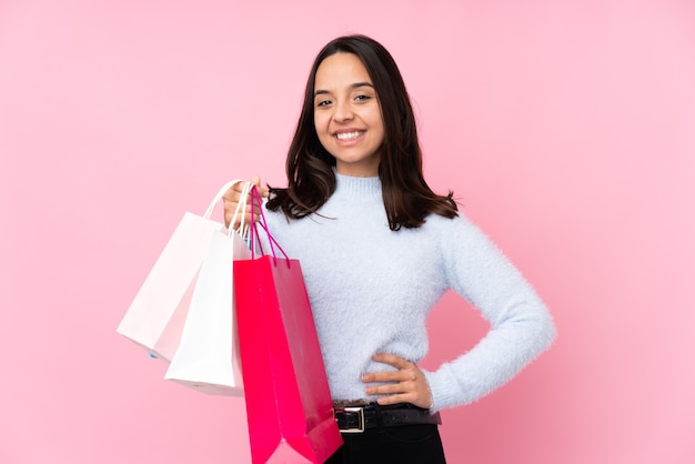 Junge Frau mit Einkaufstasche über isolierter rosa Wand, die mit den Armen an der Hüfte aufwirft und lächelt