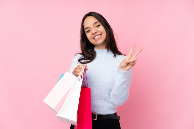 Junge Frau mit Einkaufstasche über lokalisierter rosa Wand lächelnd und Siegeszeichen zeigend
