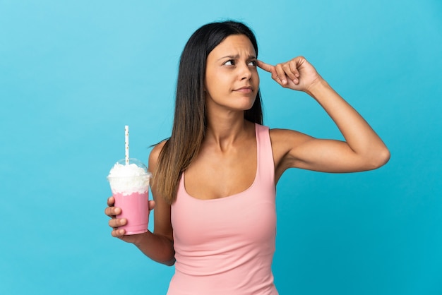 Junge Frau mit Erdbeermilchshake, der Zweifel hat und denkt