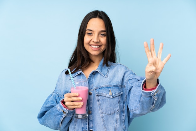 Junge Frau mit Erdbeermilchshake über blau glücklich und zählt vier mit den Fingern