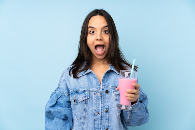 Junge Frau mit Erdbeermilchshake über isolierter blauer Wand mit überraschendem Gesichtsausdruck