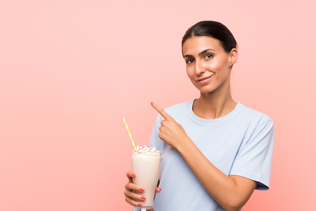 Junge Frau mit Erdbeermilchshake über lokalisierter rosa Wand zeigend auf die Seite, um ein Produkt darzustellen