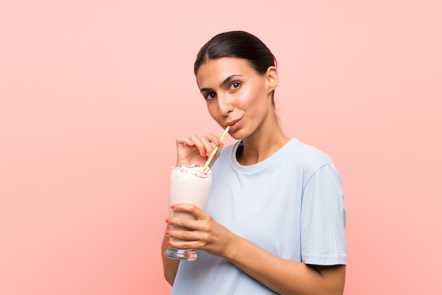 Junge Frau mit Erdbeermilchshake über lokalisierter rosa Wand