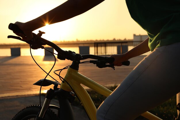 Junge Frau mit Fahrrad am Stadtufer bei Sonnenuntergang in der Nähe