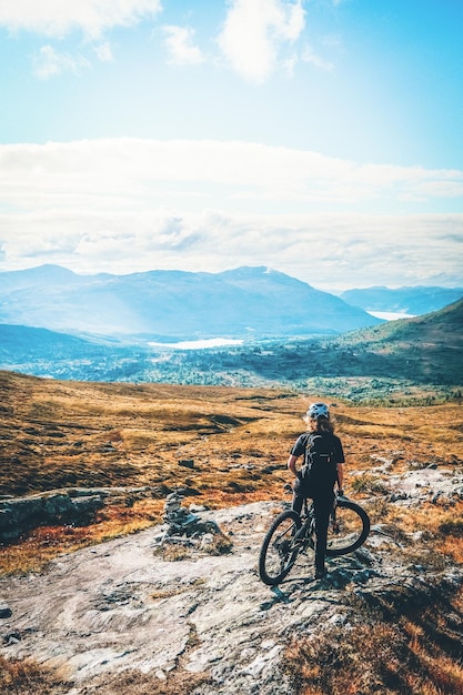 Junge Frau mit Fahrrad auf dem Feld gegen den Himmel
