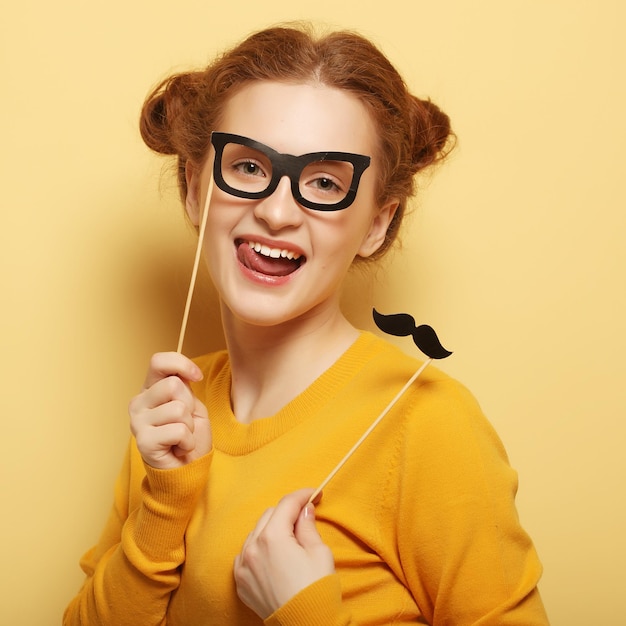 Junge Frau mit falschen Schnurrbärten und Gläsern über gelbem backgro
