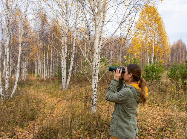 Junge Frau mit Fernglas, die Vögel im herbstlichen Wald beobachtet Wissenschaftliche Forschung Birdwathing