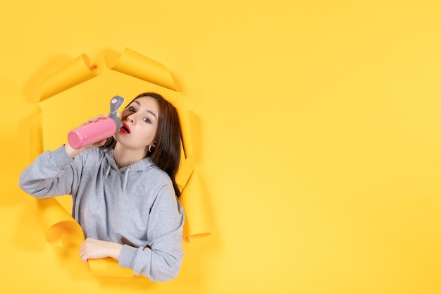 junge Frau mit Flasche Wasser auf gelbem Papierhintergrund Athlet Indoor-Fitnessstudio