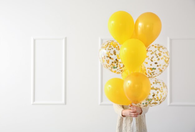 Junge Frau mit Geburtstagsballons nahe weißer Wand