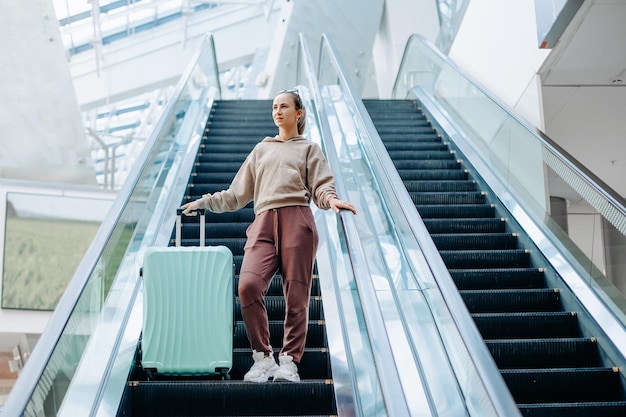 Junge Frau mit Gepäck steht auf der Rolltreppe am Flughafen