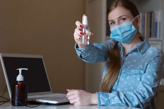 Foto junge frau mit gesichtsmaske desinfiziert geräteoberflächen an ihrem arbeitsplatz