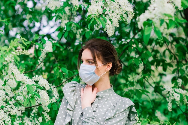 Junge Frau mit Gesichtsmaske im Freien in einem Blütengarten. Corona-Virus-Konzept.