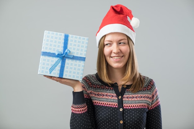 Junge Frau mit glücklichem Lächeln hält Geschenkkiste in den Händen, die über Grau isoliert ist