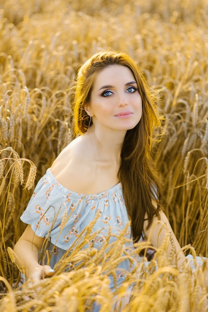 junge Frau mit großen schönen Augen hält ihre Hände auf dem Bauch und sitzt auf einem Feld von Getreide, Weizen, Roggen