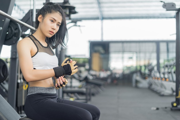 Junge Frau mit Handschuh, während sie im Fitnessstudio sitzt