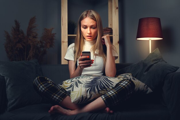 Junge Frau mit Handy. Auf der Couch sitzen. Bleiben Sie zu Hause Konzept während Coronavirus covid-2019. Nahaufnahme.