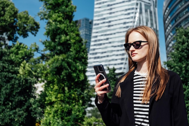 Junge Frau mit Handy auf modernen Wolkenkratzern in der Innenstadt von Wolkenkratzern mit Blick auf die Stadt