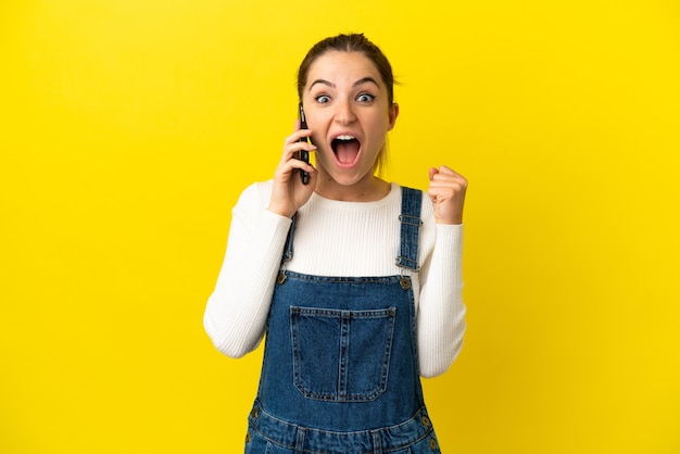 Junge Frau mit Handy über isolierten gelben Hintergrund