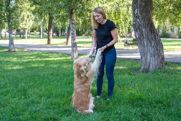 Junge Frau mit Hund Retriever im Park. Mädchen, das den Hund an den Vorderpfoten hält.