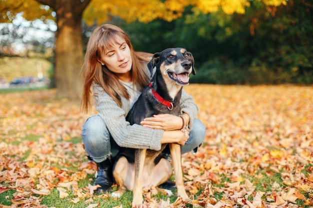 Junge Frau mit Hund sitzt im Herbst auf Blättern
