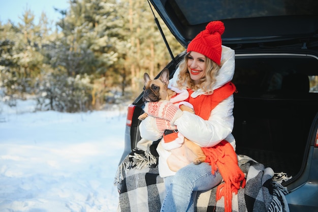 Junge Frau mit Hundesitting im offenen Kofferraum des Autos. Winterurlaub im Wald.