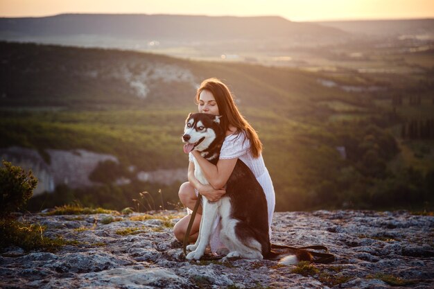 Junge Frau mit Husky-Hund an einem sonnigen Tag, der in hohen Bergen sitzt