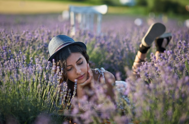 Junge Frau mit Hut, die am Sommertag im Lavendelfeld liegt