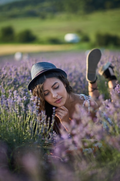 Junge Frau mit Hut, die am Sommertag im Lavendelfeld liegt
