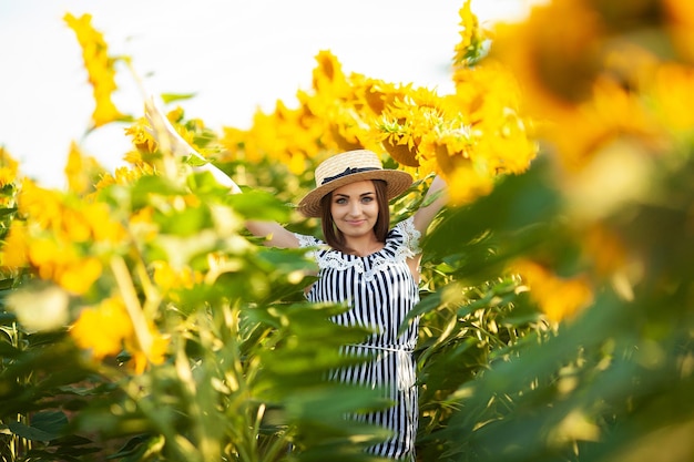 Junge Frau mit Hut genießt den Sommer im Sonnenblumenfeld bei Sonnenuntergang