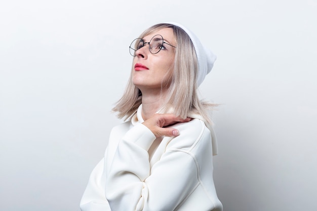 Junge Frau mit Hut mit Brille nachdenklich auf hellem Hintergrund nachschlagen.