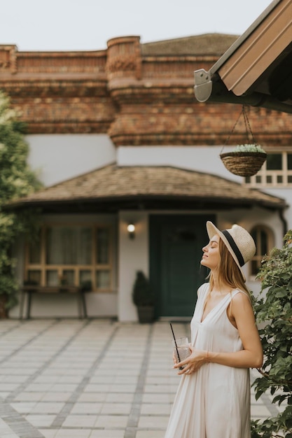 Junge Frau mit Hut trinkt kalte Limonade im Garten des Resorts