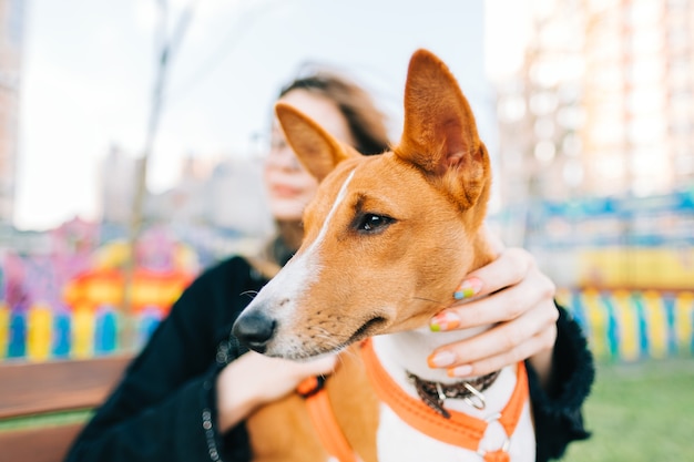 Junge Frau mit ihrem Basenji-Hund sitzt auf einer Bank im Stadtpark.